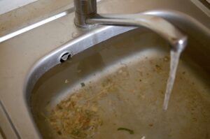 Agujero de tapón de fregadero de acero inoxidable cerca lleno de agua y partículas de alimentos - Desatascos Madrid